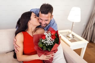 Beautiful young couple at home. Hugging, kissing and enjoying spending time together while celebrating Saint Valentine's Day with red roses