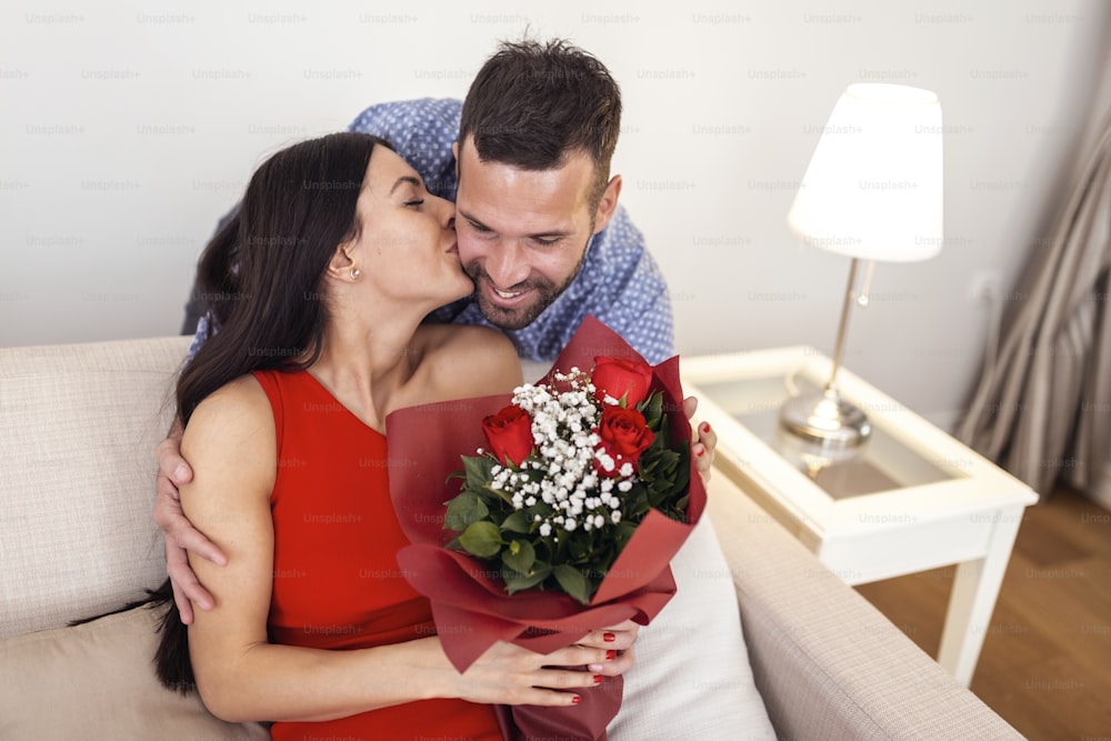 Beautiful young couple at home. Hugging, kissing and enjoying spending time together while celebrating Saint Valentine's Day with red roses