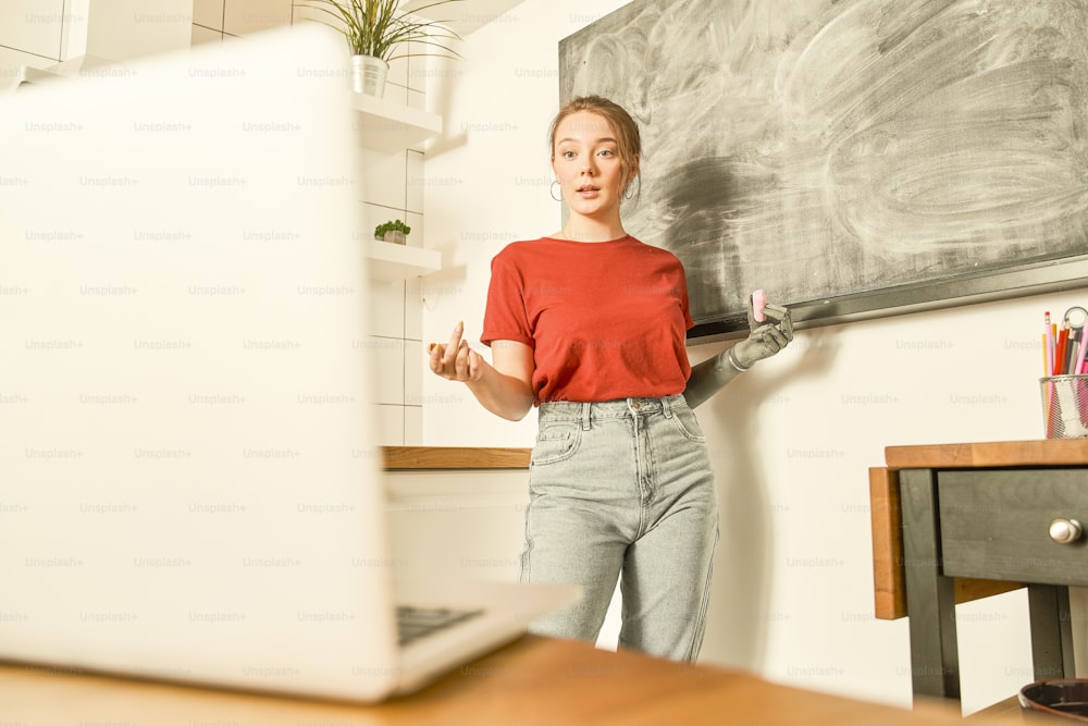 Creative woman with artificial limb answering at the teacher question correctly while standing in front of the chalkboard. Girl demonstrating something while drawing on the board. Remote education concept