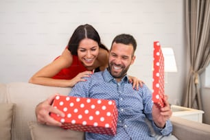 Beautiful smiling young couple celebrating love for Valentine's day or anniversary. Attractive woman surprising him with a present.