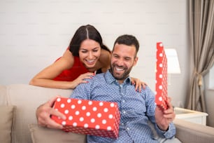 Schönes lächelndes junges Paar, das die Liebe zum Valentinstag oder Jahrestag feiert. Attraktive Frau, die ihn mit einem Geschenk überrascht.