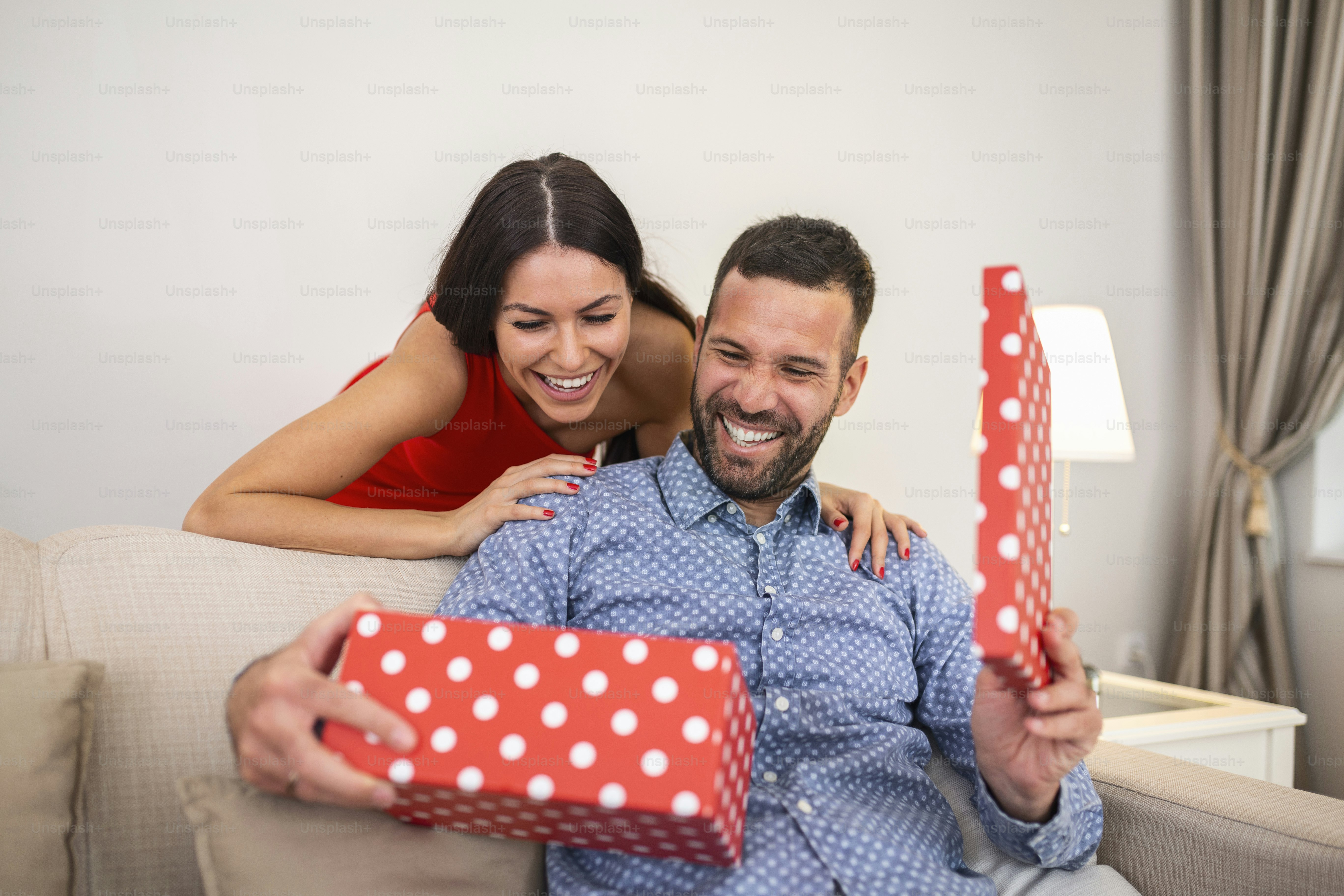 Beautiful smiling young couple celebrating love for Valentine's day or anniversary. Attractive woman surprising him with a present