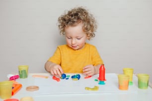 Cute Caucasian blond curly baby boy child playing with sensor kinetic toy playdough. Hand brain development activity for young toddler kids. Early age preschool education.