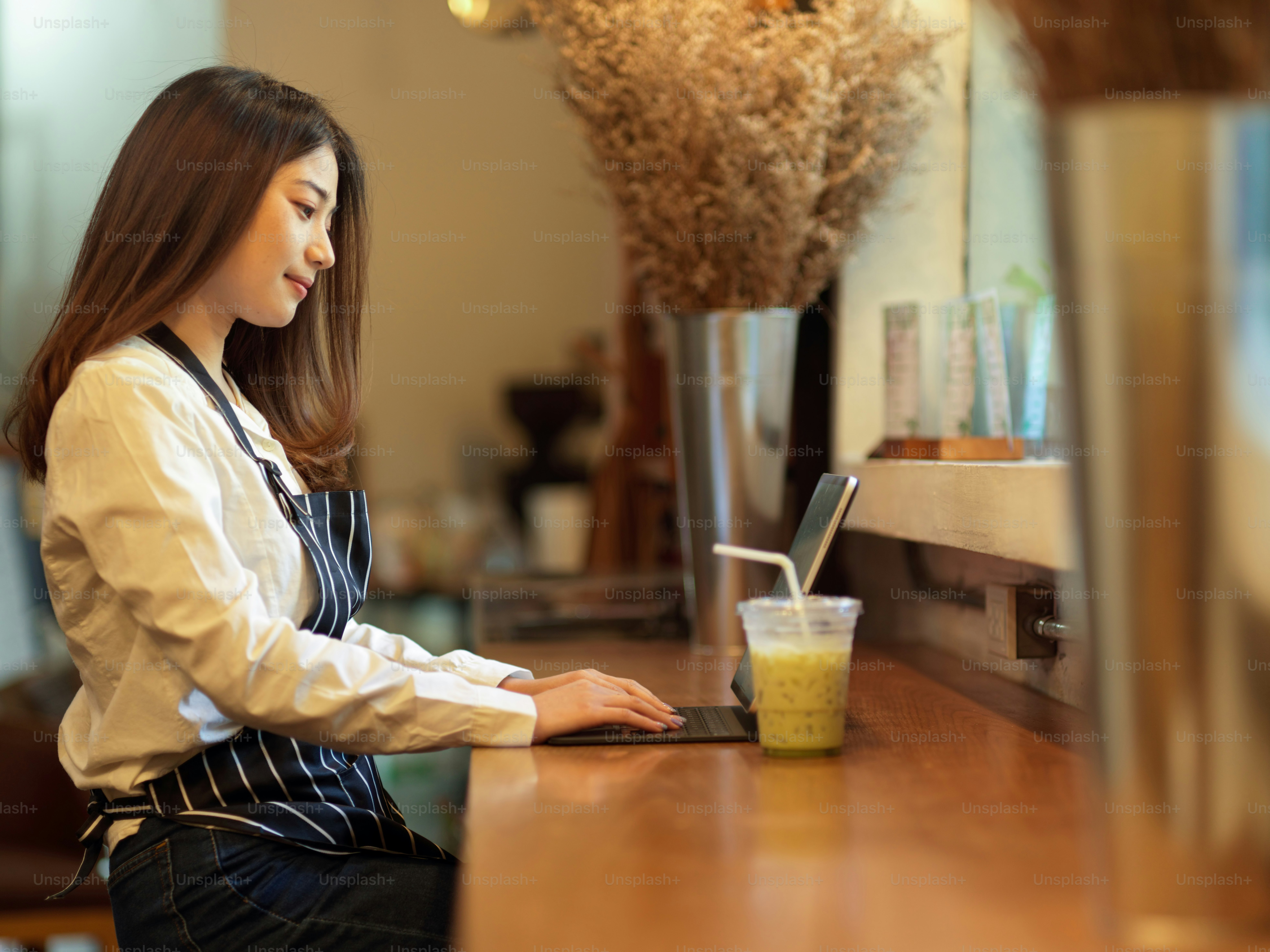Side view of female barista relaxing from work with digital tablet on wooden bar in cafe
