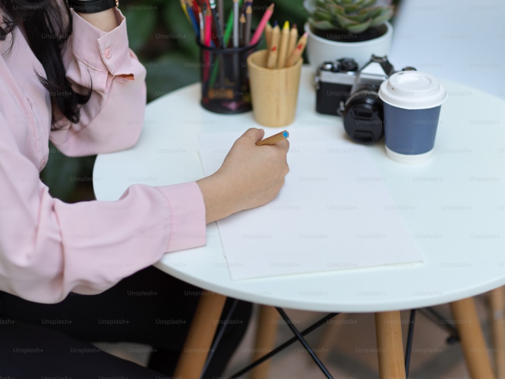 카페의 커피 테이블에 있는 모형 종이에 손으로 그림을 그리는 여학생의 자른 샷