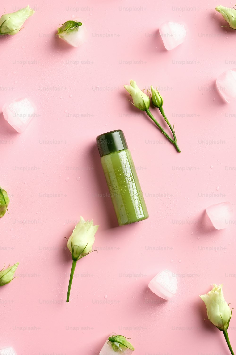 Shower gel green clear cosmetic bottle, ice cubes, spring flowers on pink background. Natural beauty product. Flat lay, top view.