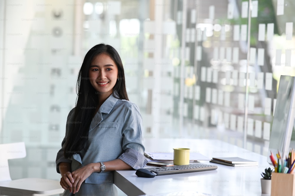 Portrait of cheerful businesswoman standing near her workplace.