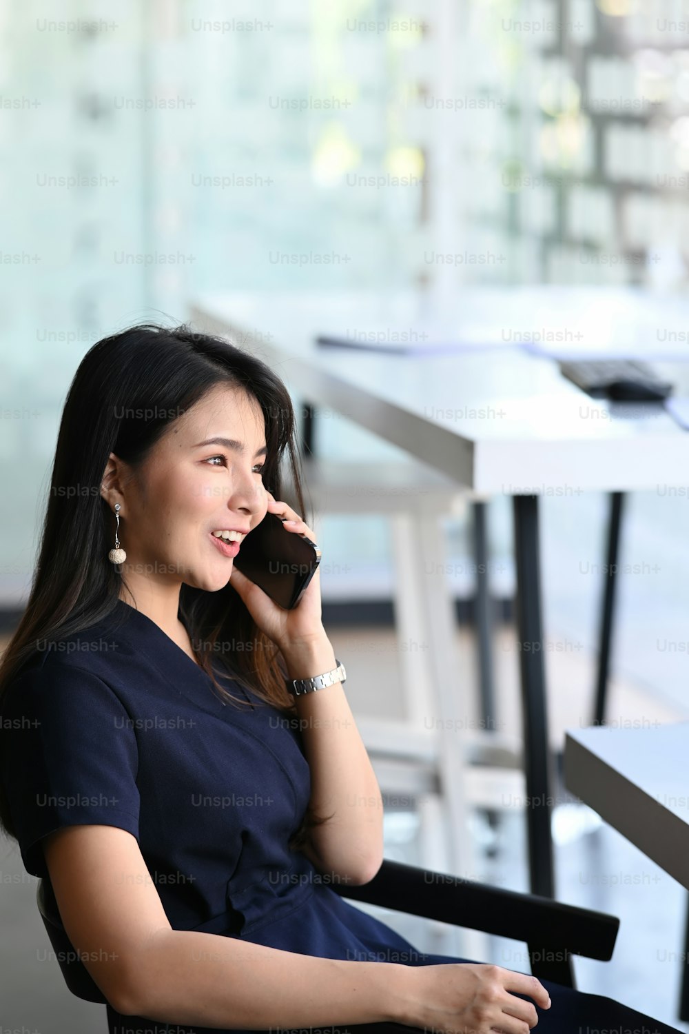 Beautiful businesswoman looking through window and talking on mobile phone at office.