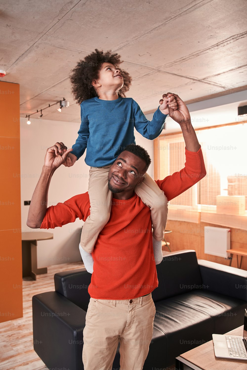 Happy childhood. Calm multiracial father holding at the shoulders his little curly son and playing with him at the living room. Father and son relationships concept. Stock photo
