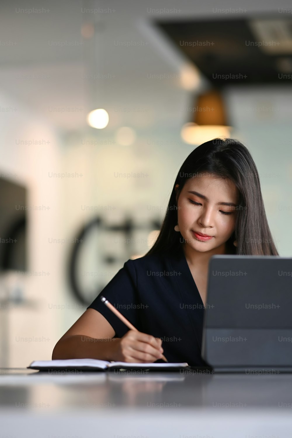 Portrait of businesswoman using tablet computer and writing information on notebook.