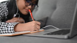 Close up view of Asian girl student during online courses on laptop computer while lying on sofa at home.