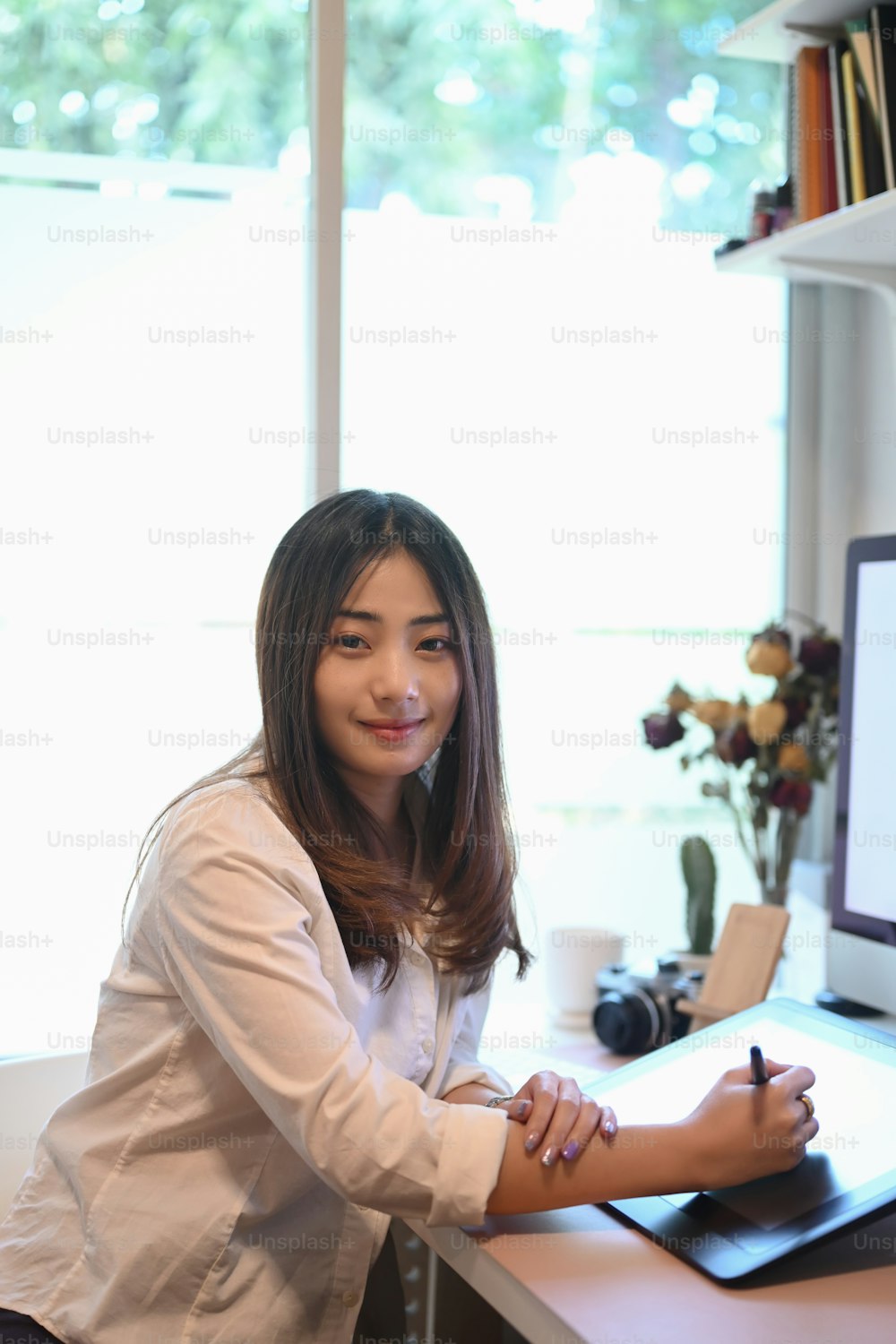Young woman designer using graphics tablet and smiling to camera at creative workplace.