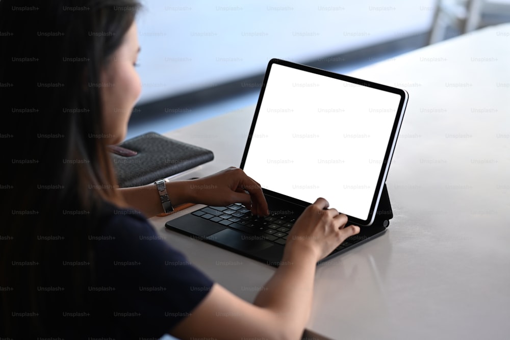 Rear view of female freelancer working on tablet computer while sitting at comfortable workplace.