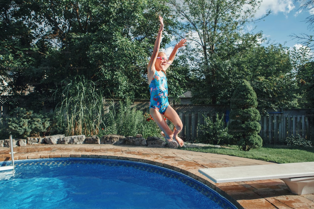 Menina criança mergulhando pulando na água na piscina do quintal da casa. Criança engraçada e bonita desfrutando e se divertindo na piscina no dia de verão. Atividade aquática ao ar livre de verão para crianças.