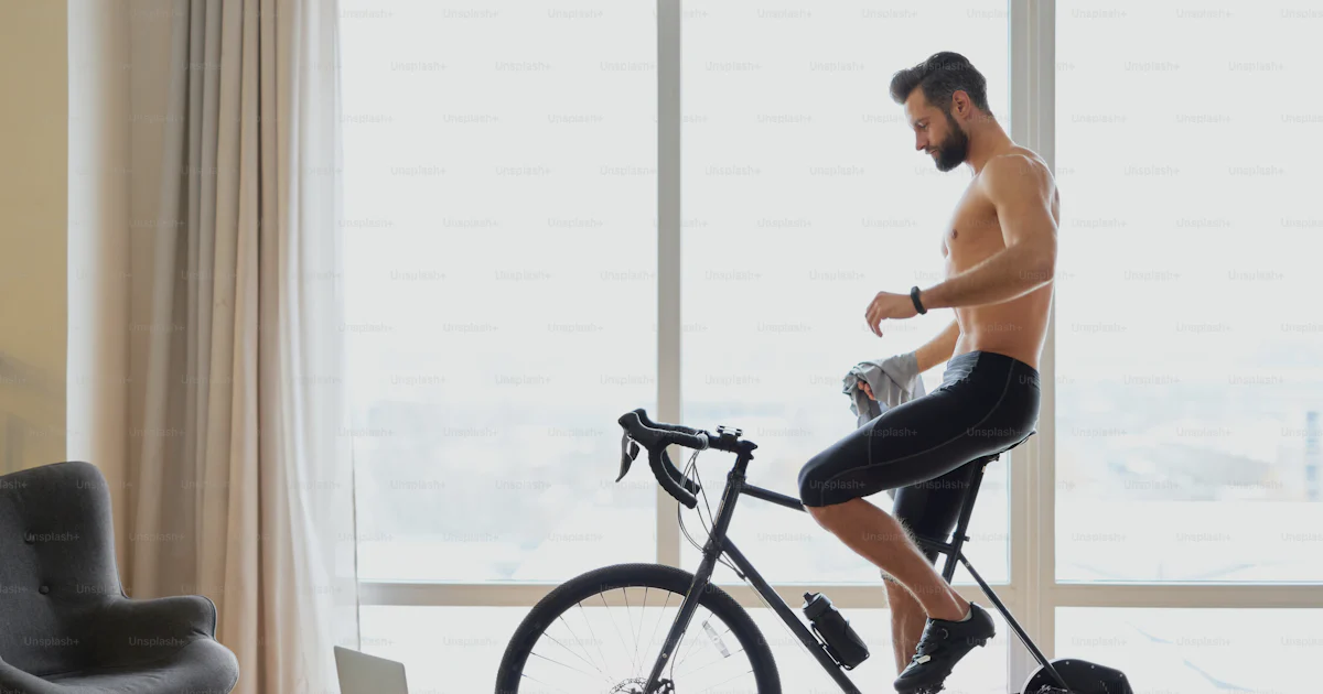 Exercise Bike Rider Muscular young man riding stationary exercise bike in room with laptop ...