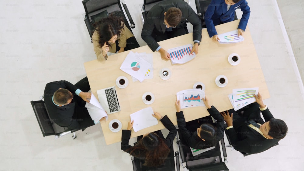 オフィスで上から見たビジネスパーソングループミーティング。専門職のビジネスウーマン、ビジネスマン、オフィスワーカーは、会議テーブル上のプロジェクト計画文書を使用してチーム会議に参加しています。