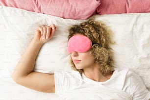 Hermosa mujer durmiendo con una venda rosa en los ojos en la cama