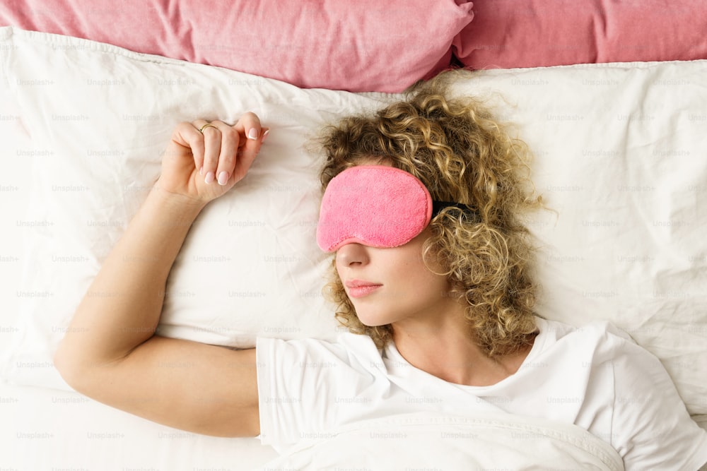 Mulher bonita dormindo com uma venda rosa em seus olhos na cama