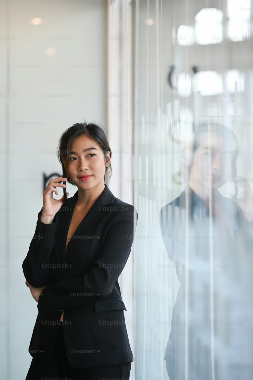 Portrait of businesswoman in suit talking on phone and looking away near the window in office.