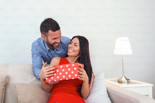 Schönes junges Paar feiert zu Hause. Ein gutaussehender Mann schenkt seiner Freundin eine Geschenkbox. Valentinstag Konzept