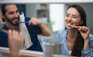 Retrato de jovem casal escovando os dentes na frente do espelho dentro de casa.