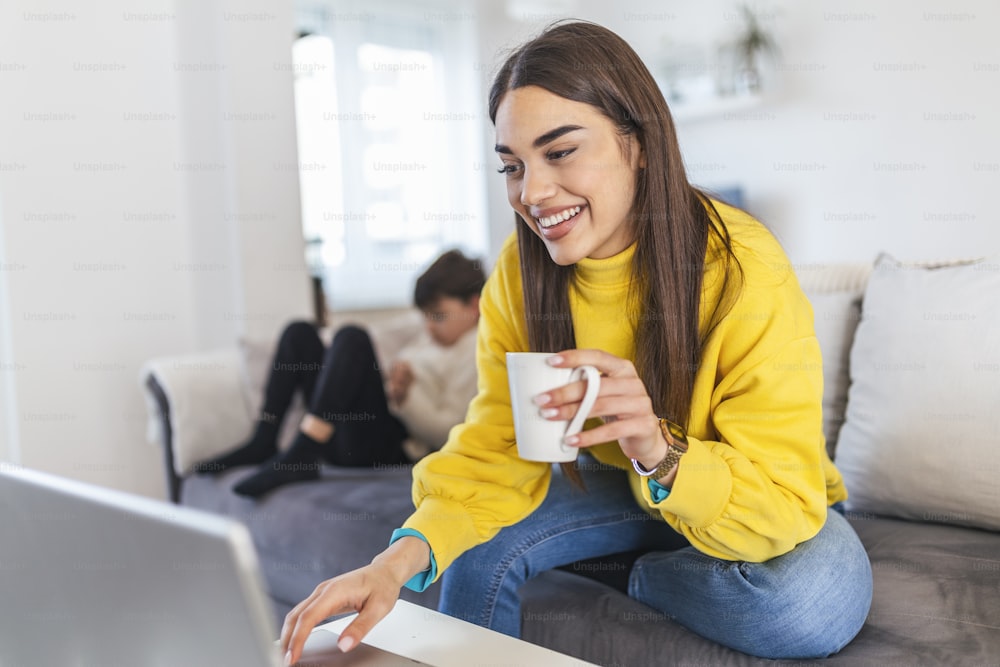 Millennial generation mother working from home with small children while in quarantine isolation during the Covid-19 health crisis. Little boy on tablet computer.