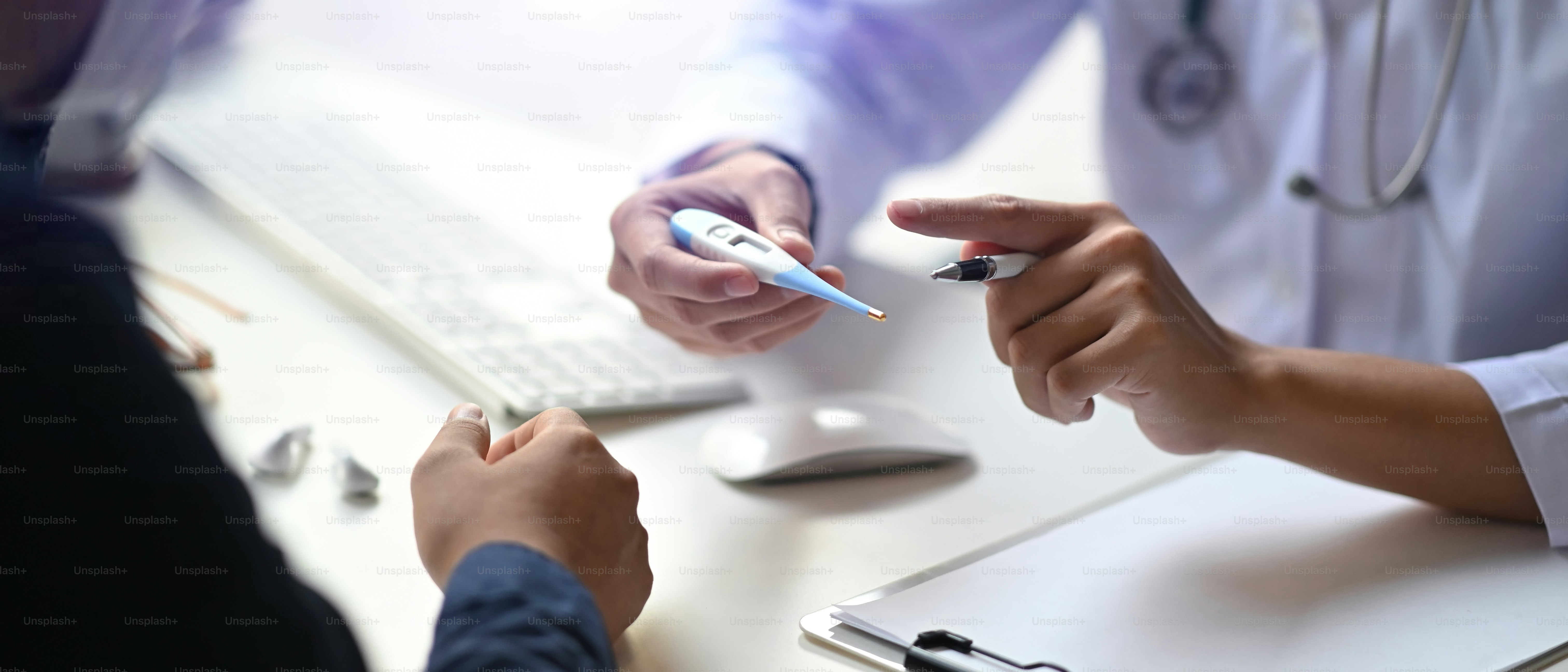 デジタル体温計を持ち、患者と話す医師の接写。