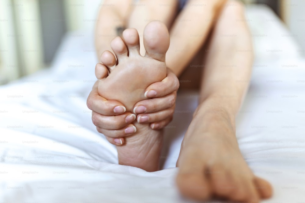 Foot Pain woman sitting on the bed holding her feet at home having painful feet and stretching muscles fatigue To relieve pain. Health concept.