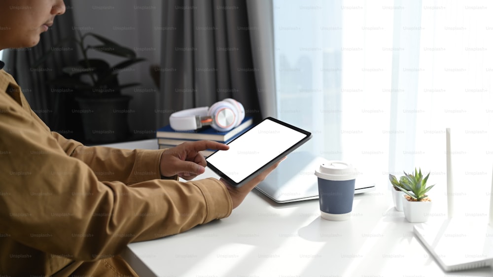 Vista lateral do jovem sentado no local de trabalho confortável e usando o tablet digital durante o trabalho on-line.