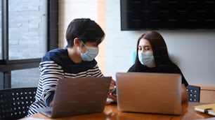 Two young creative designer in protective masks works together in the office.