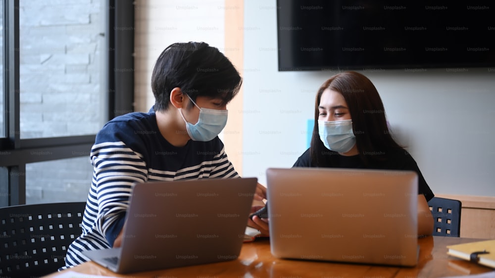 Two young creative designer in protective masks works together in the office.
