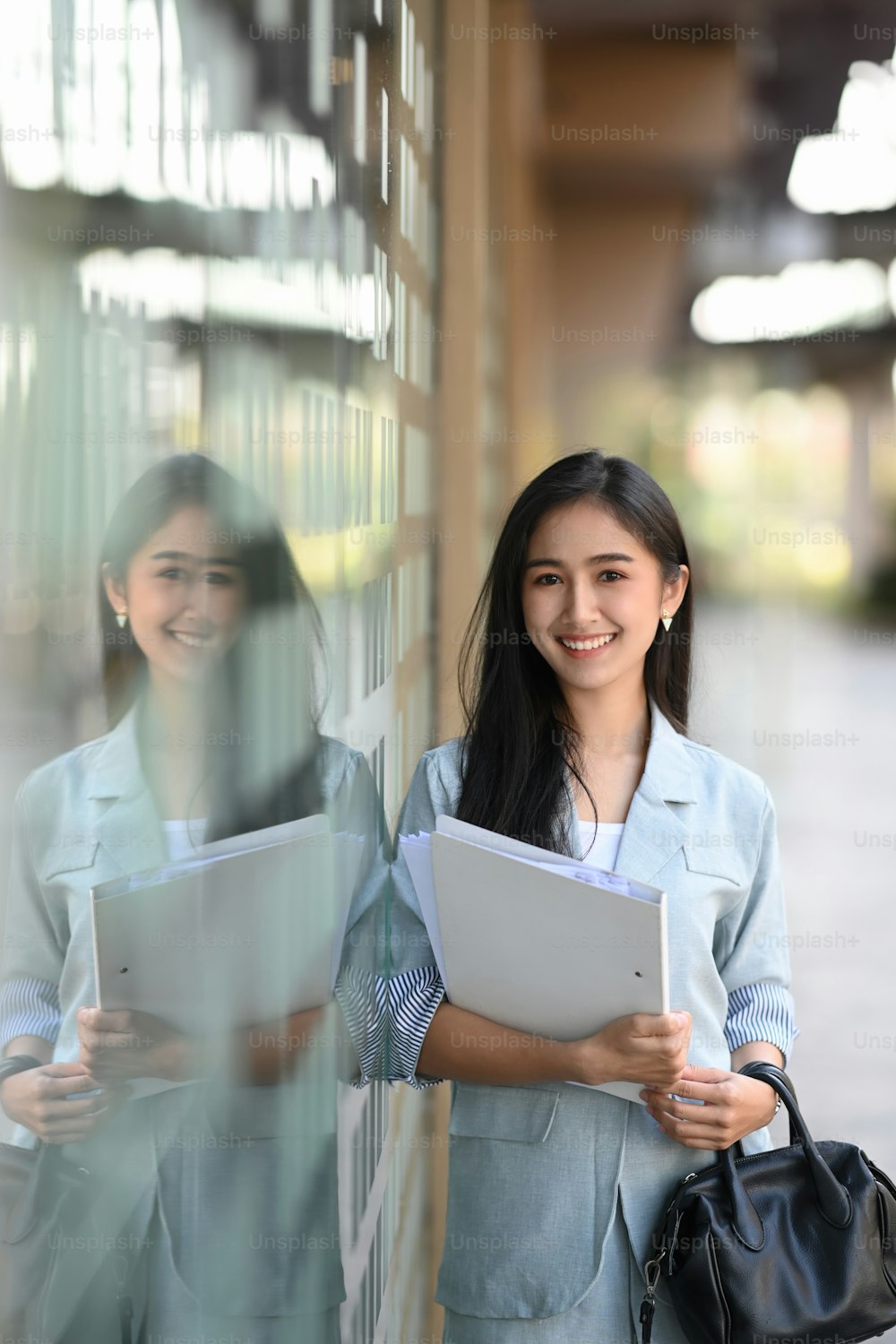 Retrato de una mujer de negocios asiática sosteniendo una carpeta de documentos y de pie fuera del edificio de oficinas.