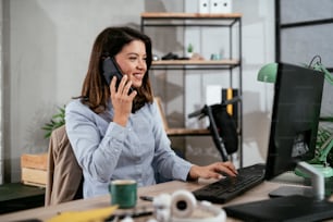 Empresária usando o telefone no escritório. Bela jovem mulher que trabalha no computador em seu local de trabalho.