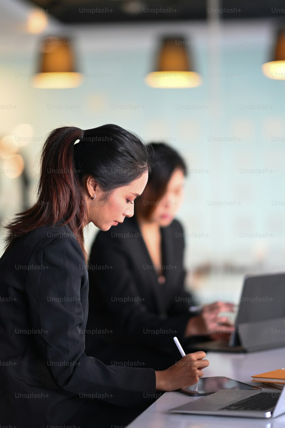 Two female colleagues in office co working and working with tablet computer.