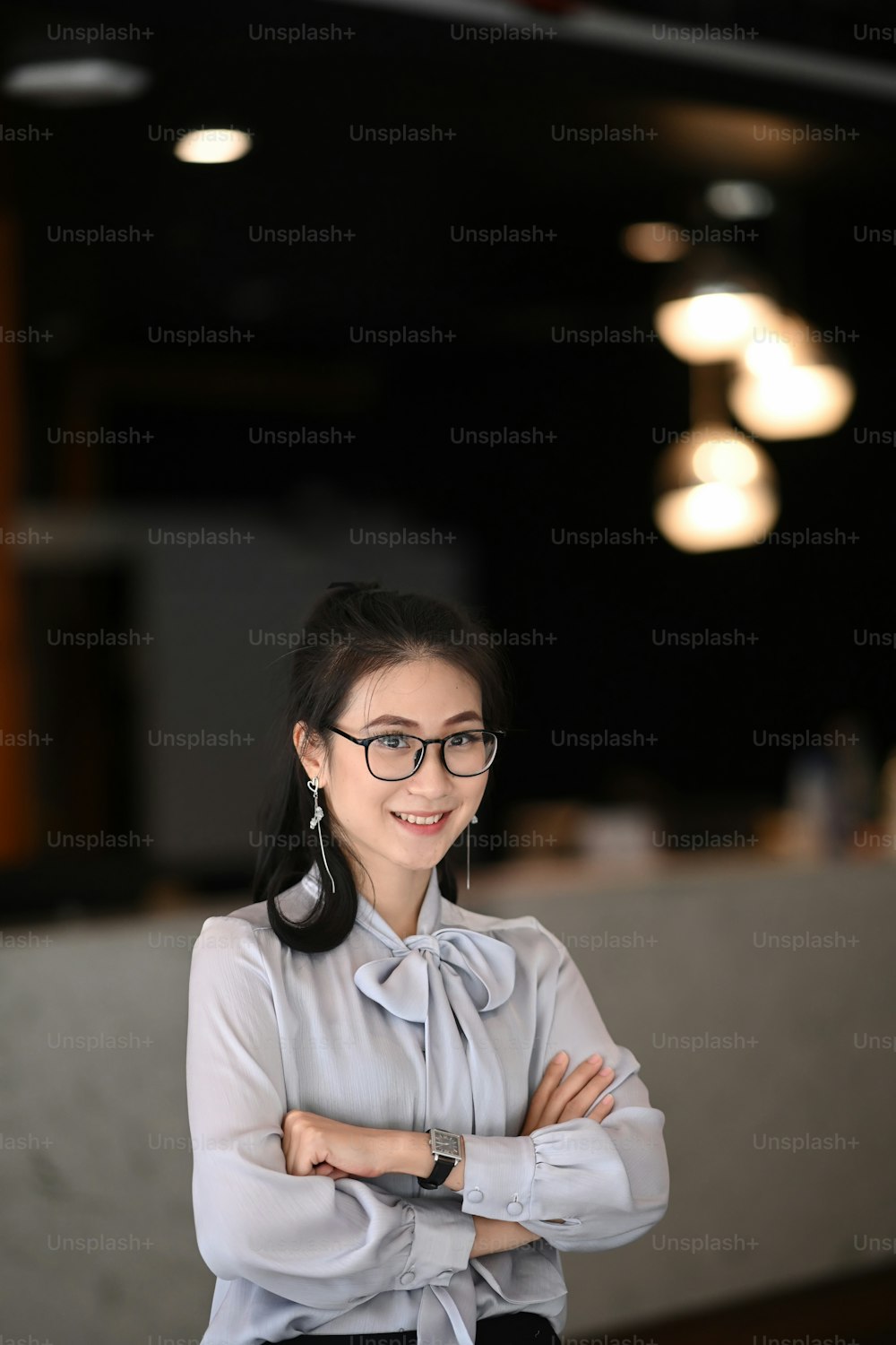 Portrait of confident businesswoman standing with arm crossed in modern office and smiling to camera.