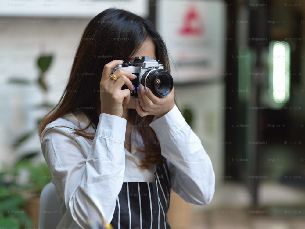 Portrait d’une femme photographe prenant une photo avec un appareil photo numérique dans un café