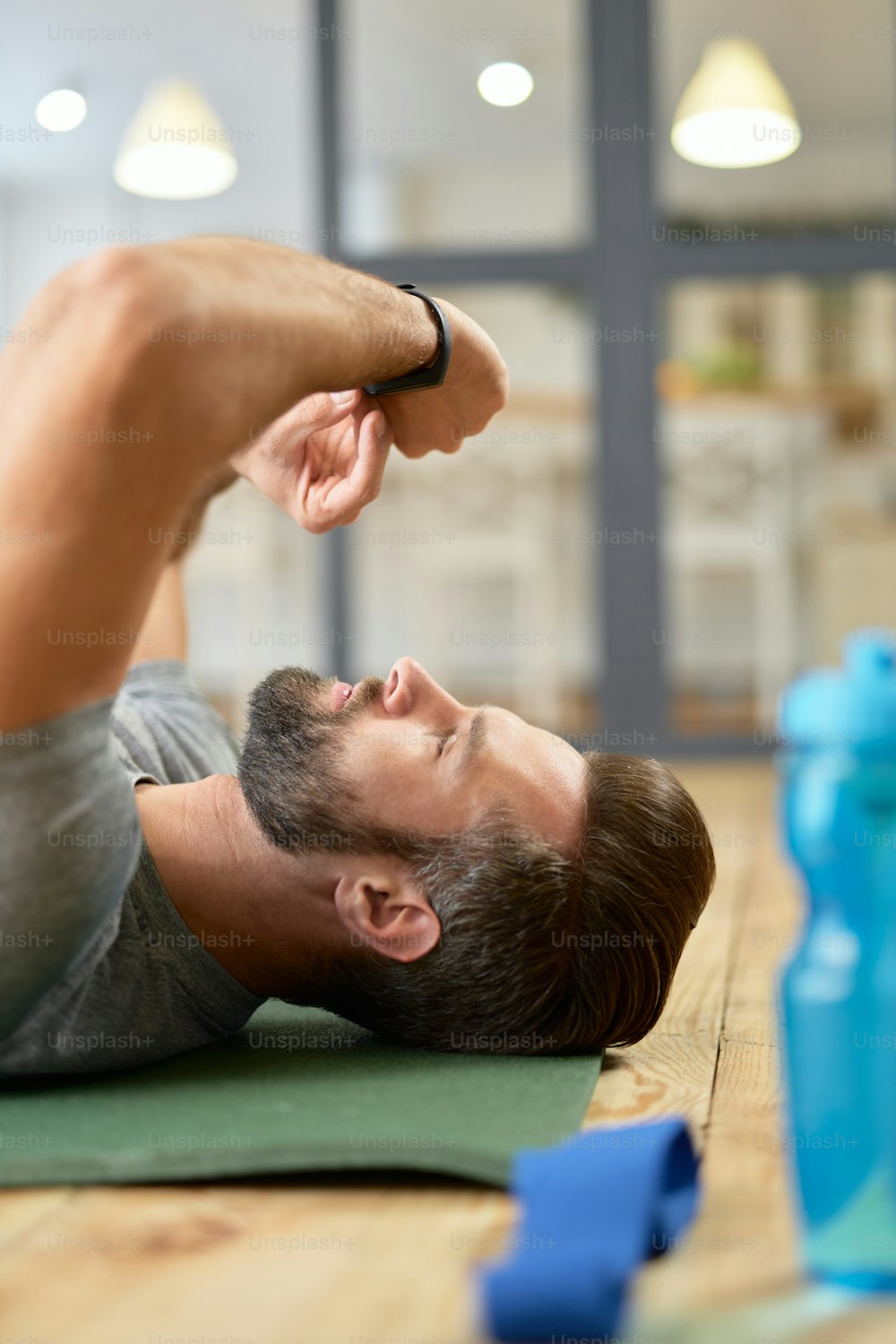 Handsome gentleman lying on exercise mat and looking at modern wearable gadget on his wrist