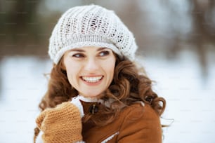 mulher moderna sorridente com luvas em um chapéu de malha e casaco de pele de carneiro ao ar livre no parque da cidade no inverno.