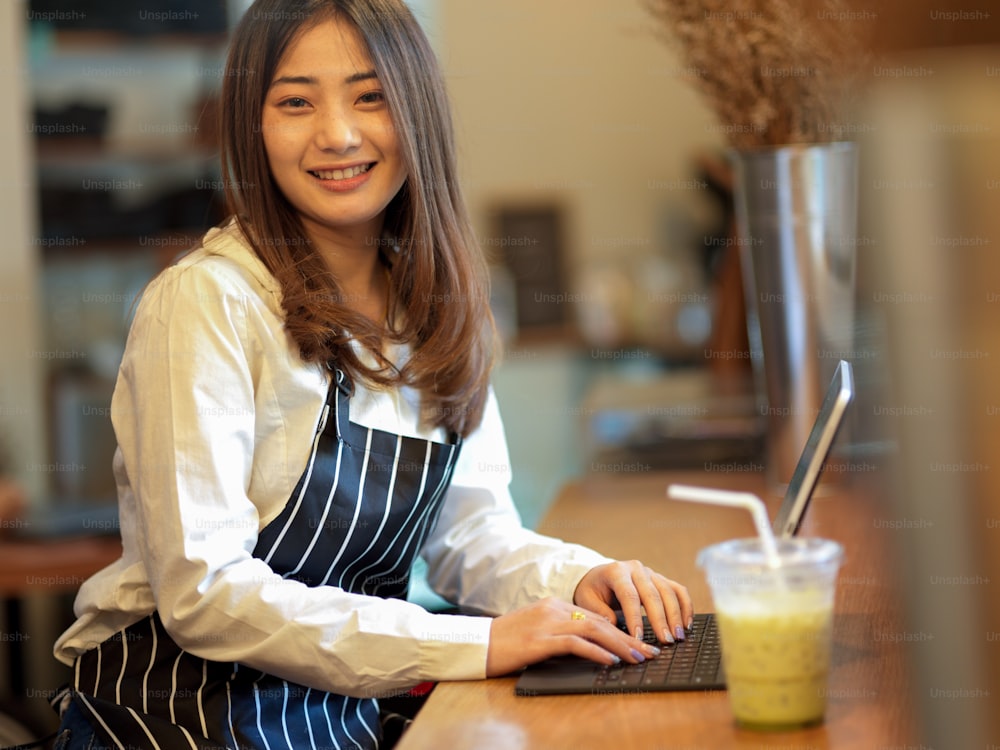 Portrait of female barista smiling to camera while relaxing from work with digital tablet in cafe