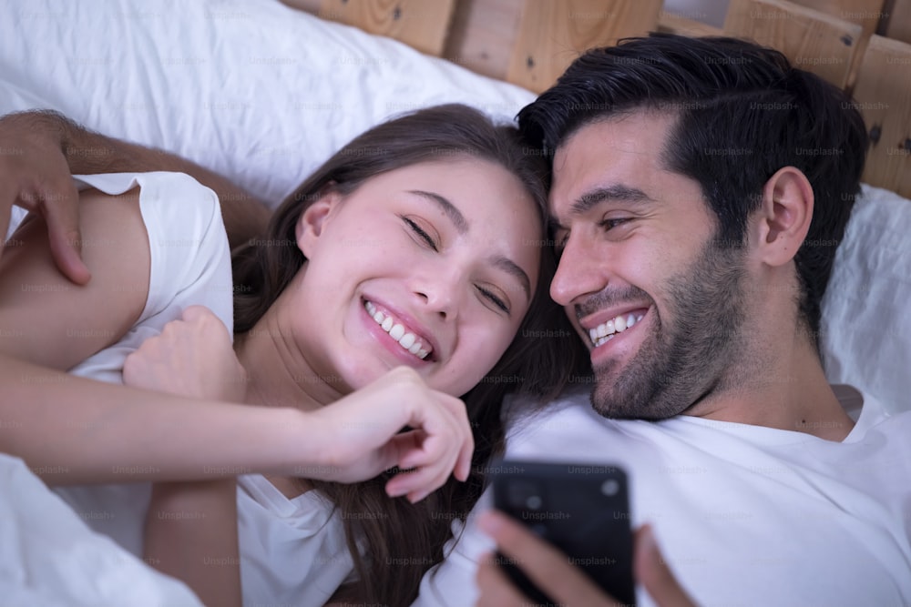 携帯電話を持つベッドの若いカップル