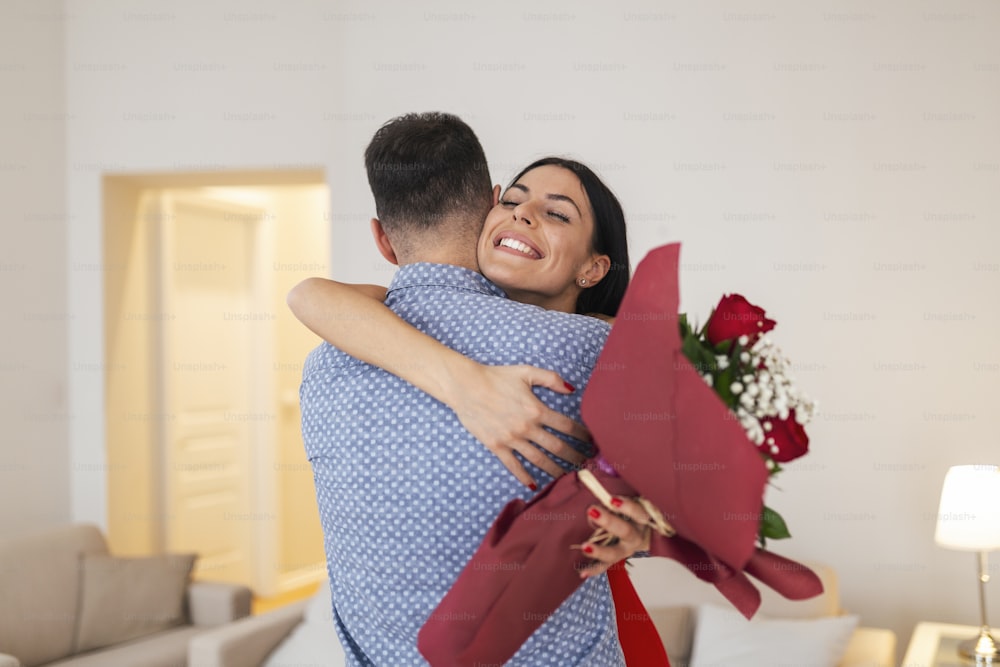 Valentine's Day concept. Happy couple in love with. A young loving couple celebrating Valentine's Day. Lovers hugging each other. Handsome man surprises his girlfriend with red roses at home