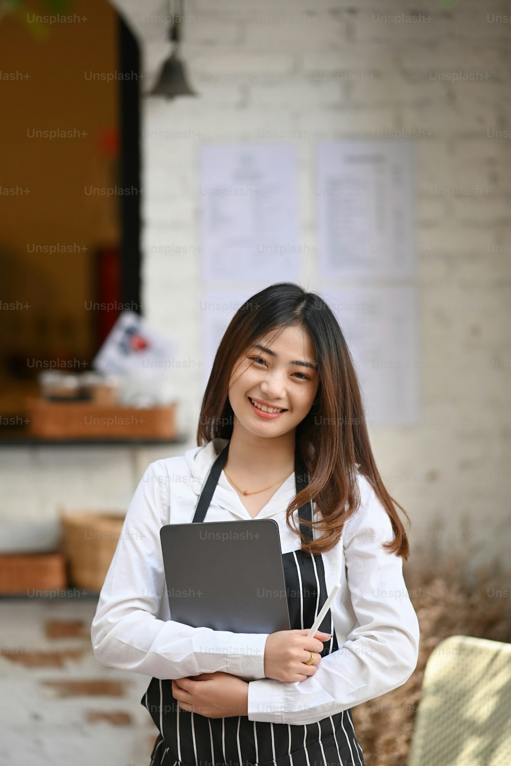 Portrait of happy waitress standing at coffee shop and holding digital tablet.