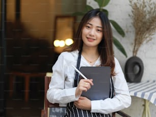 Portrait of waitress smiling to camera and holding digital tablet ready to take order in restaurant