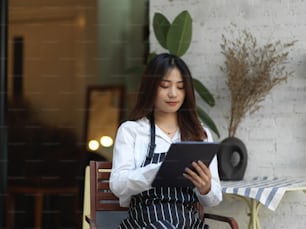 Ritratto di giovane bella cameriera che prende un ordine sulla tavoletta digitale di fronte al caffè