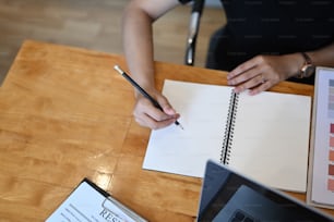 Overhead shot of young woman holding pen writing on empty notebook on wooden table.