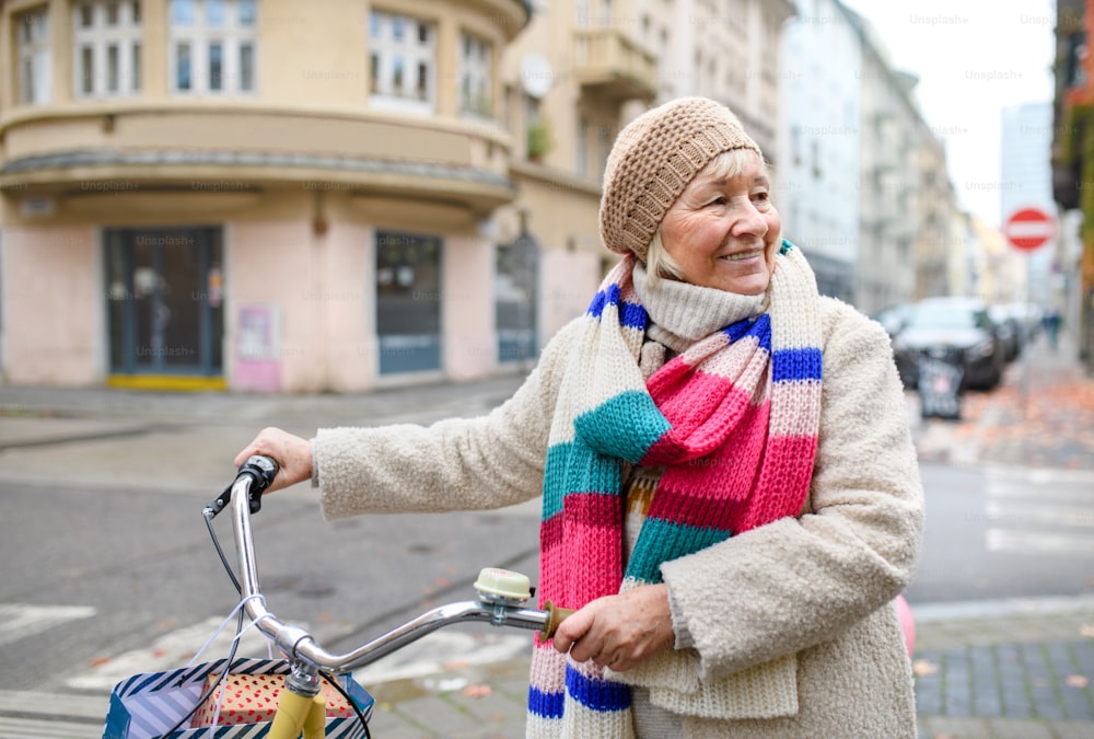 Portrait of senior woman with bicycle crossing road outdoors in city.