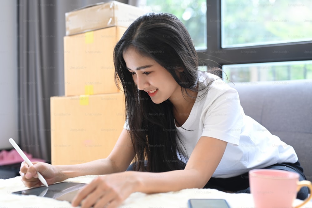 Smiling young business start up online seller owner using digital tablet for checking the customer orders at home.