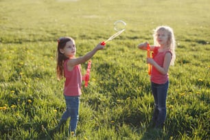 Happy Caucasian girls blowing soap bubbles in park on summer day. Kids having fun outdoor. Authentic happy childhood magic moment. Lifestyle seasonal activity for children.
