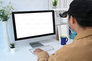 Vista posteriore del giovane che utilizza il computer moderno durante il lavoro online a casa.