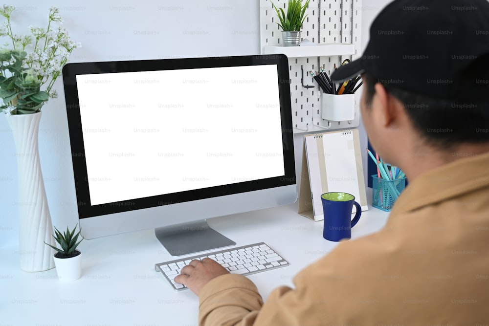 Rückansicht eines jungen Mannes, der einen modernen Computer benutzt, während er zu Hause online arbeitet.